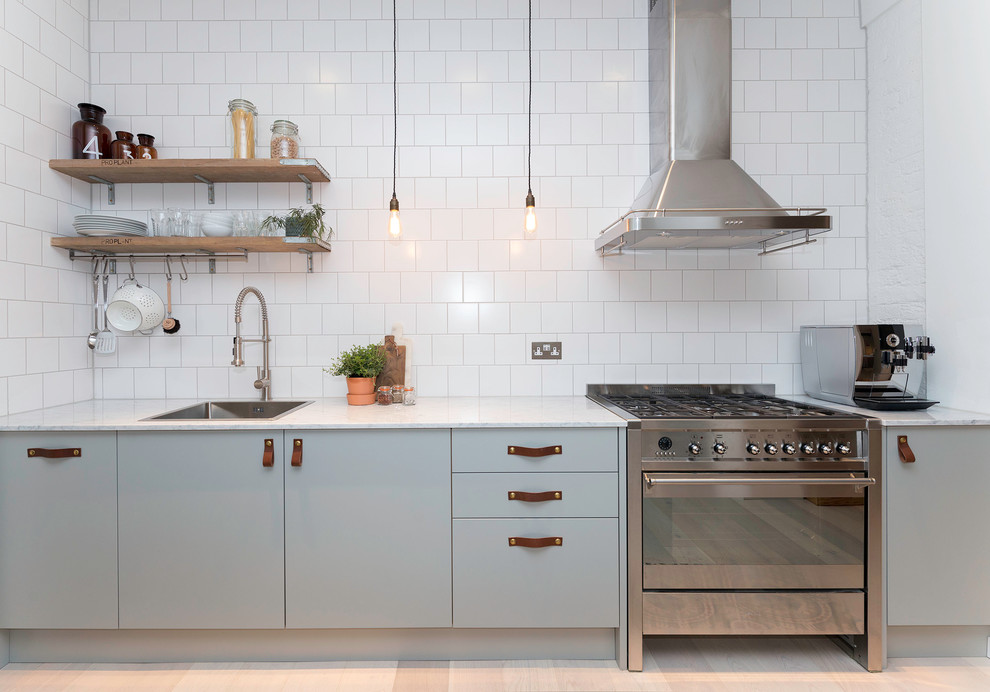 Example of a danish light wood floor kitchen design in London with a drop-in sink, flat-panel cabinets, blue cabinets, white backsplash, subway tile backsplash and stainless steel appliances