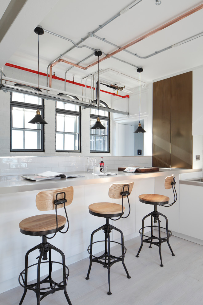 Photo of an industrial kitchen in London with white splashback, metro tiled splashback and light hardwood flooring.