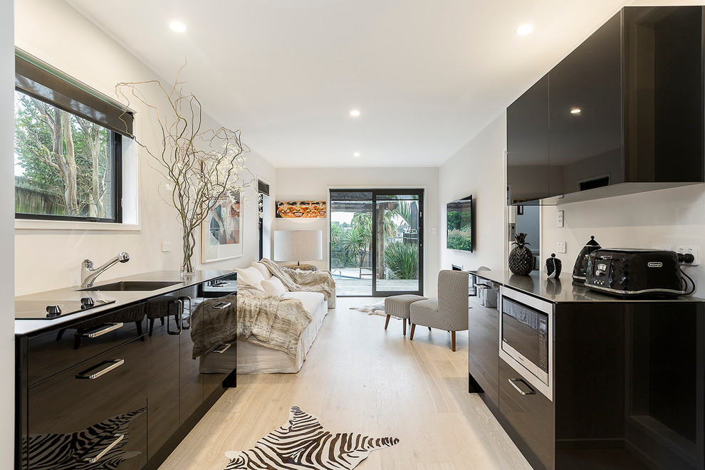 Photo of a small modern galley open plan kitchen in Auckland with an integrated sink, flat-panel cabinets, black cabinets, stainless steel worktops, laminate floors, no island and beige floors.
