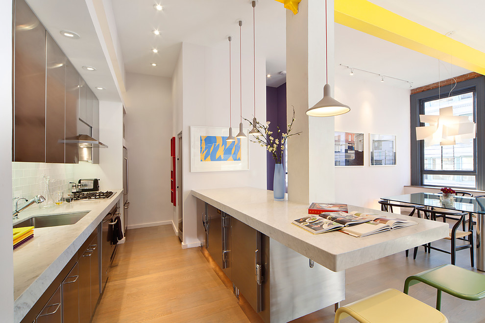Photo of a medium sized contemporary galley kitchen/diner in New York with a submerged sink, flat-panel cabinets, stainless steel cabinets, granite worktops, glass tiled splashback, stainless steel appliances, medium hardwood flooring and a breakfast bar.