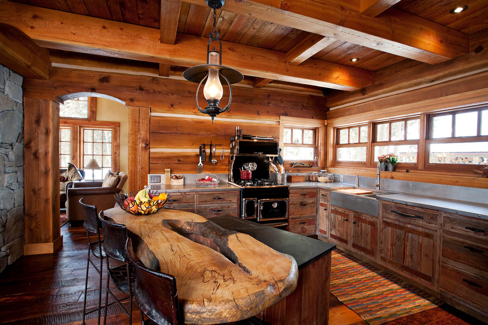 Foto på ett rustikt l-kök, med skåp i slitet trä, bänkskiva i rostfritt stål, svarta vitvaror, mörkt trägolv, en köksö och en rustik diskho