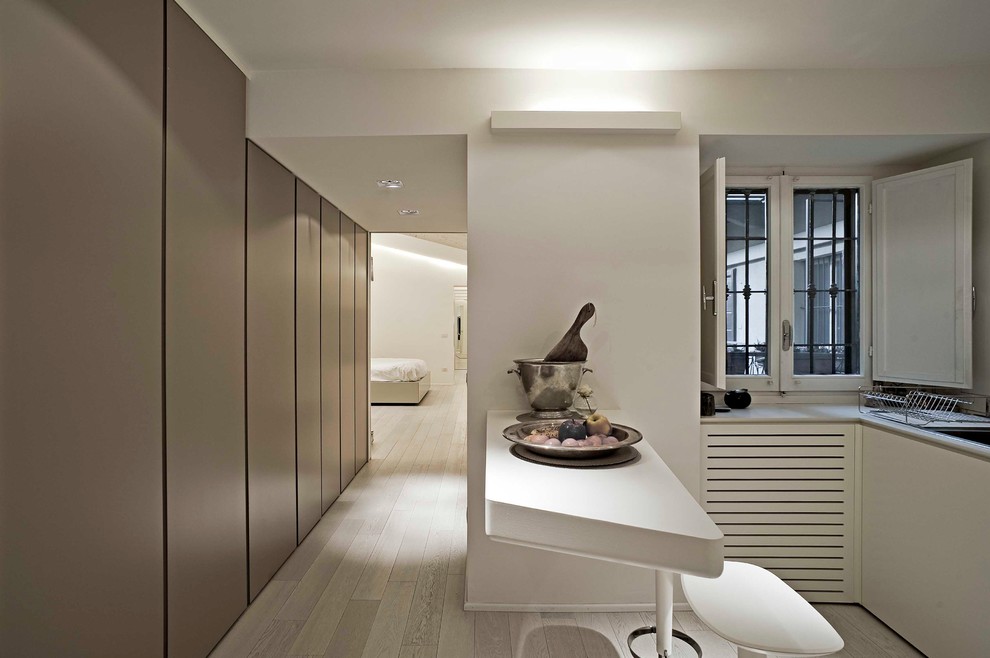 Imagen de cocina contemporánea abierta con armarios con paneles lisos, puertas de armario blancas, encimera de acrílico y suelo de madera clara