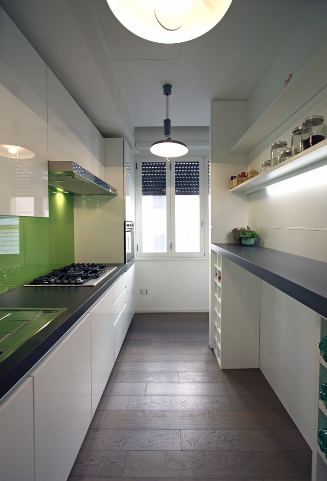Modern inredning av ett litet kök, med en nedsänkt diskho, släta luckor, vita skåp, bänkskiva i kvarts, grönt stänkskydd, glaspanel som stänkskydd, rostfria vitvaror, mellanmörkt trägolv och en köksö