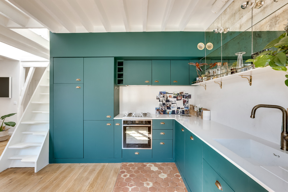パリにある高級な広いコンテンポラリースタイルのおしゃれなキッチン (緑のキャビネット、アイランドなし、一体型シンク、フラットパネル扉のキャビネット、白いキッチンパネル、黒い調理設備、淡色無垢フローリング、白いキッチンカウンター、茶色い床) の写真