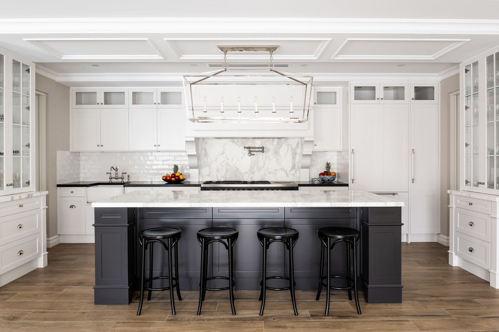 Immagine di una cucina chic con lavello stile country, ante con riquadro incassato, ante bianche, paraspruzzi bianco, pavimento in legno massello medio, pavimento marrone e top bianco