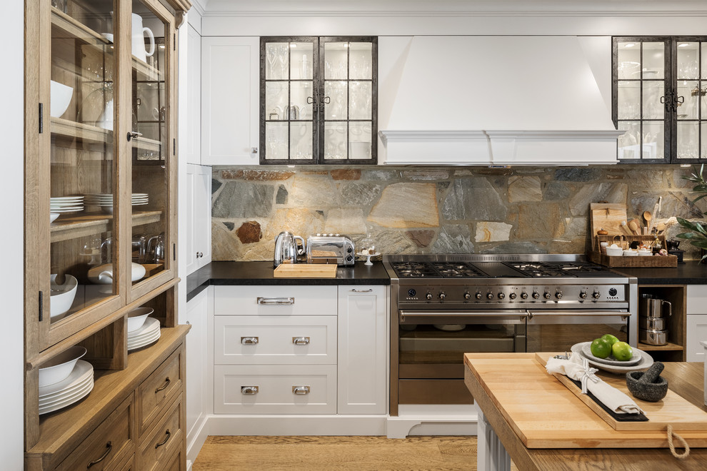 This is an example of a large rustic kitchen in Perth with shaker cabinets, granite worktops, brown splashback, stainless steel appliances, medium hardwood flooring, an island, black worktops, white cabinets and slate splashback.