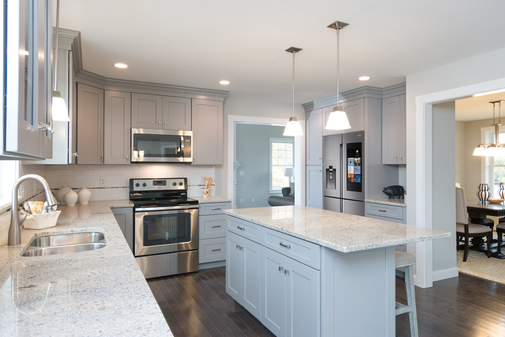 Example of a classic dark wood floor and brown floor enclosed kitchen design in Boston with a double-bowl sink, shaker cabinets, gray cabinets, quartzite countertops, white backsplash, subway tile backsplash, stainless steel appliances and an island