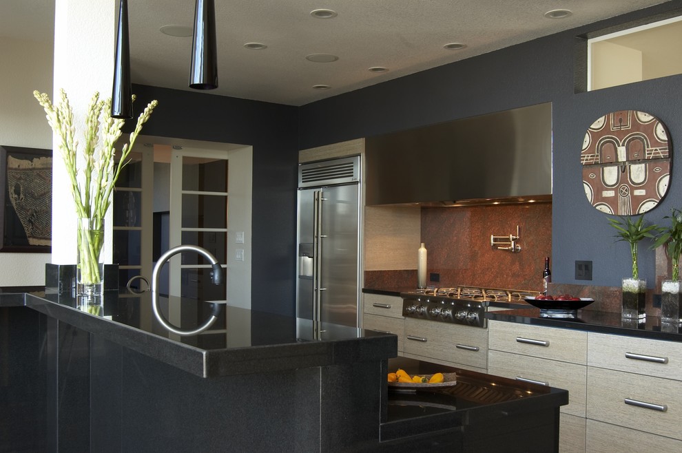 Cette image montre une cuisine parallèle design en bois clair avec un placard à porte plane, une crédence rouge, une crédence en dalle de pierre et un électroménager en acier inoxydable.