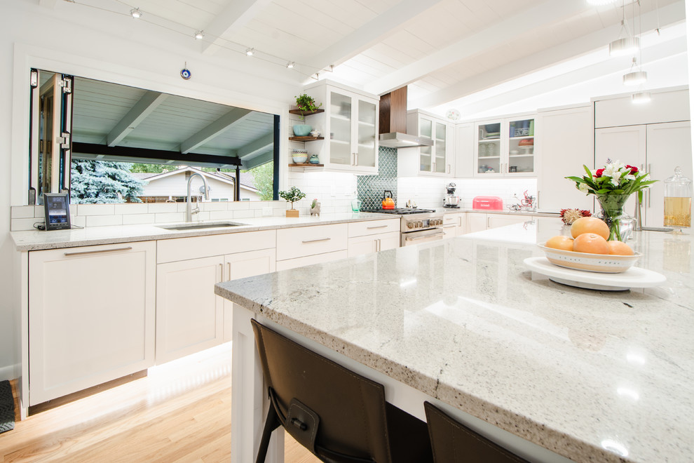 Photo of a large midcentury l-shaped kitchen/diner in Denver with a submerged sink, shaker cabinets, white cabinets, granite worktops, green splashback, mosaic tiled splashback, integrated appliances, light hardwood flooring, an island and grey worktops.