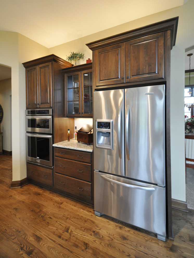Exemple d'une grande cuisine américaine linéaire chic en bois foncé avec un placard avec porte à panneau surélevé, un plan de travail en granite, un électroménager en acier inoxydable, un sol en bois brun et îlot.