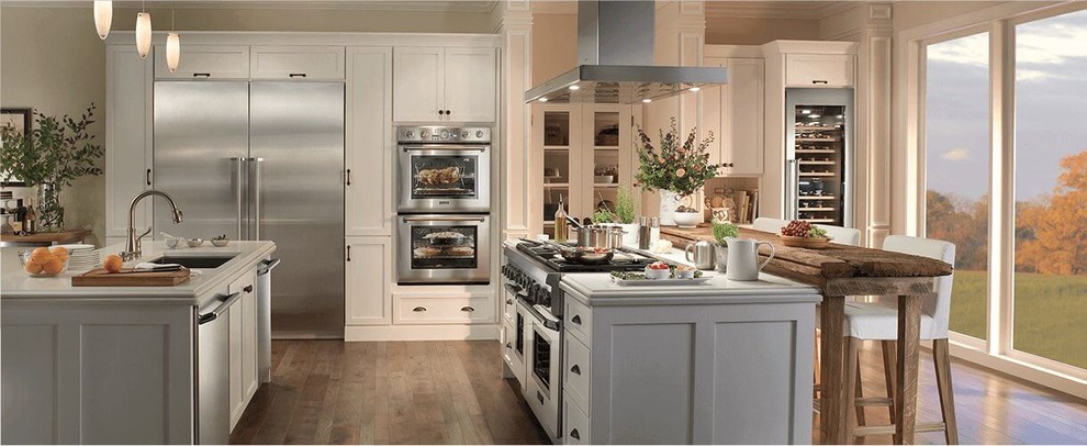 Large classic kitchen in New Orleans with a submerged sink, recessed-panel cabinets, white cabinets, stainless steel appliances, medium hardwood flooring, multiple islands, brown floors and white worktops.