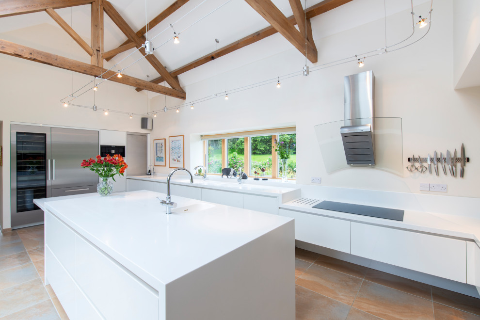 Inspiration for a large contemporary u-shaped open plan kitchen in Cheshire with an integrated sink, flat-panel cabinets, white cabinets, stainless steel appliances, terracotta flooring, an island, beige floors, white worktops, exposed beams and a vaulted ceiling.