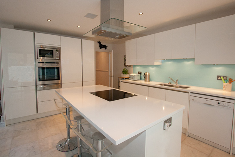 Kitchen - contemporary kitchen idea in London with white cabinets, blue backsplash, glass sheet backsplash and an island