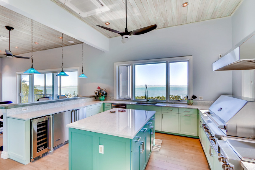 Open concept kitchen - mid-sized coastal u-shaped porcelain tile and brown floor open concept kitchen idea in Tampa with an undermount sink, shaker cabinets, turquoise cabinets, quartz countertops, white backsplash, mosaic tile backsplash, stainless steel appliances and an island
