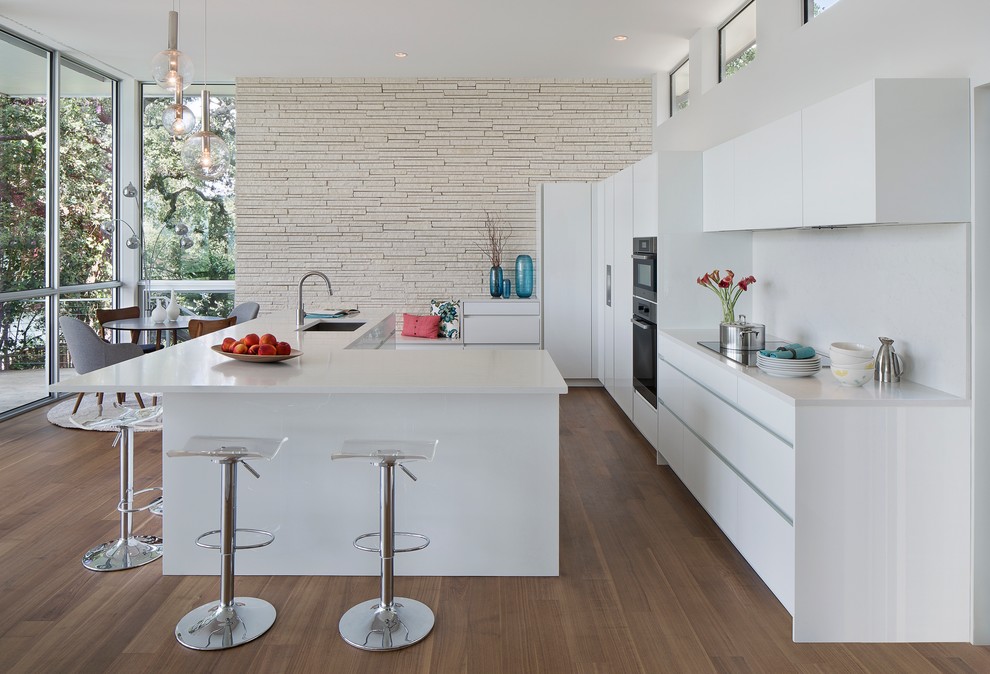 Cette image montre une cuisine encastrable design avec un évier encastré, un placard à porte plane, des portes de placard blanches, une crédence blanche, un sol en bois brun et îlot.