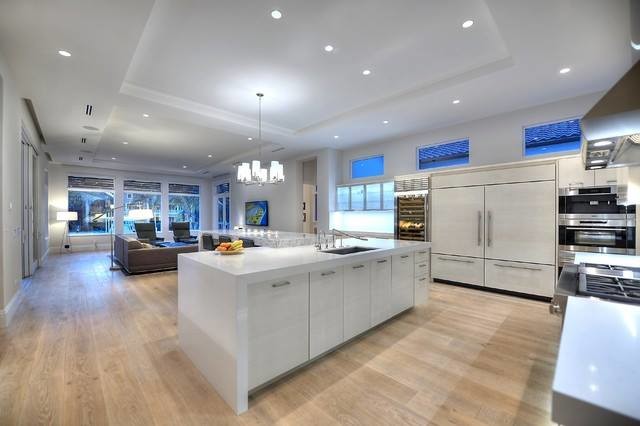 Inspiration for a large contemporary l-shaped open plan kitchen in Other with flat-panel cabinets, white cabinets, composite countertops, white splashback, integrated appliances, light hardwood flooring and multiple islands.