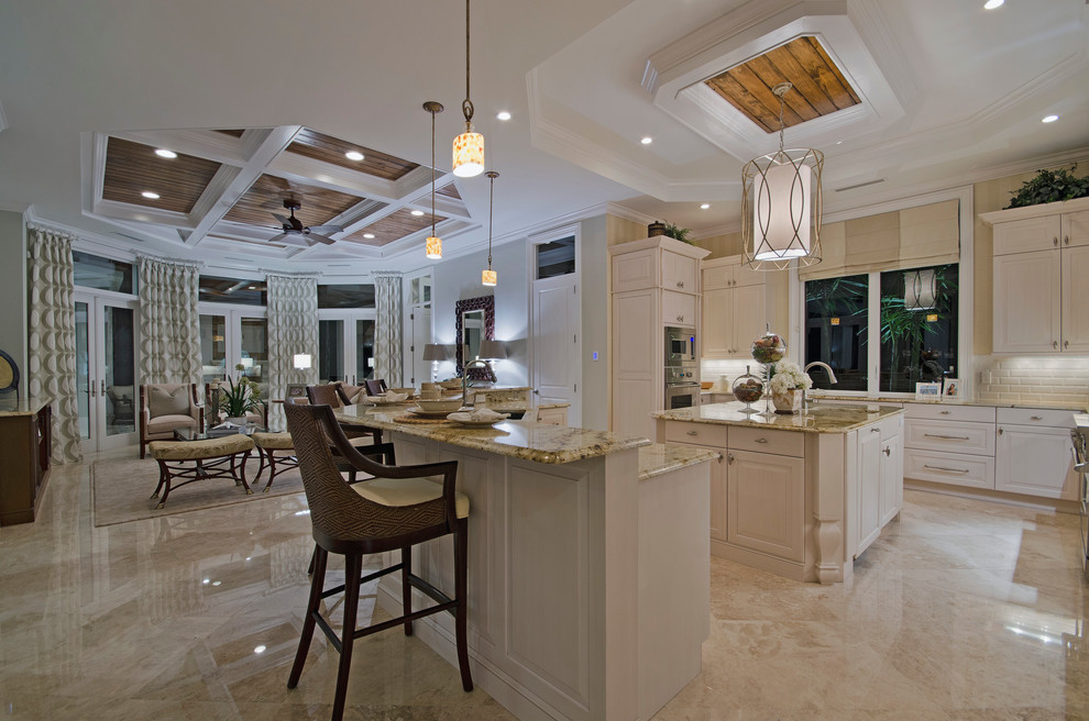 Huge beach style u-shaped marble floor open concept kitchen photo in Miami with a drop-in sink, flat-panel cabinets, white cabinets, granite countertops, white backsplash, subway tile backsplash, stainless steel appliances and an island