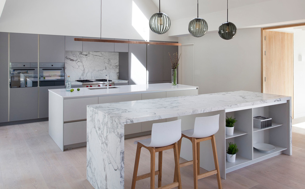 Example of a large trendy single-wall light wood floor and brown floor open concept kitchen design in Other with an integrated sink, flat-panel cabinets, green cabinets, marble countertops, gray backsplash, marble backsplash, black appliances and two islands