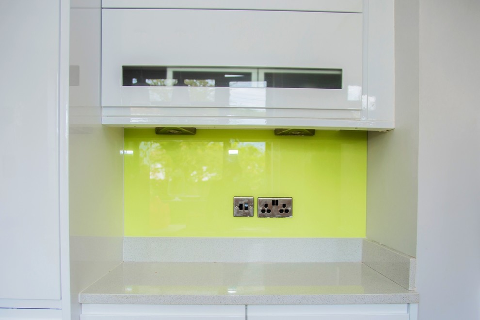 Bild på ett funkis kök, med gult stänkskydd och glaspanel som stänkskydd