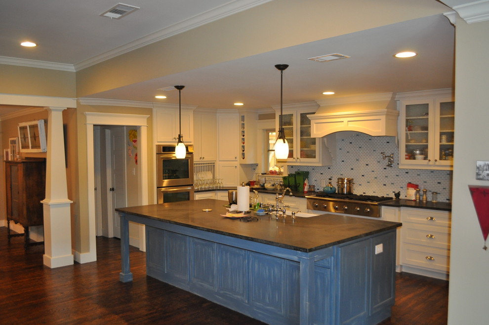 Example of an arts and crafts u-shaped medium tone wood floor open concept kitchen design in Dallas with a farmhouse sink, shaker cabinets, white cabinets, granite countertops, beige backsplash, ceramic backsplash, stainless steel appliances and an island