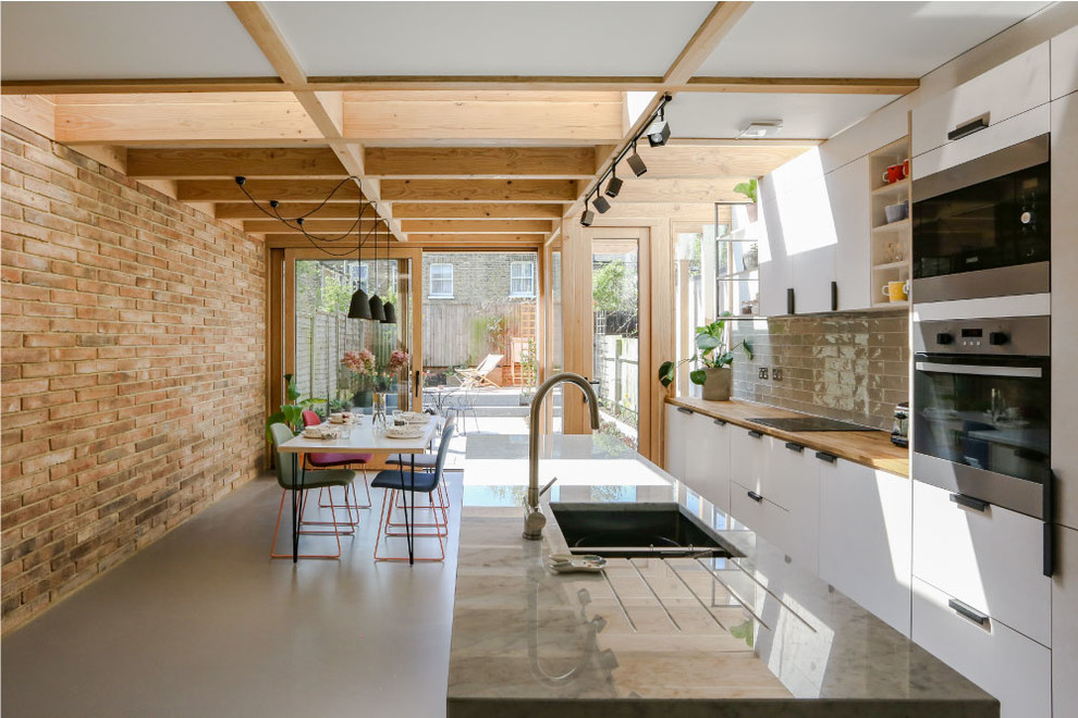 Exempel på ett industriellt kök med öppen planlösning, med en undermonterad diskho, släta luckor, vita skåp, stänkskydd i glaskakel, rostfria vitvaror, betonggolv, en köksö och grått golv
