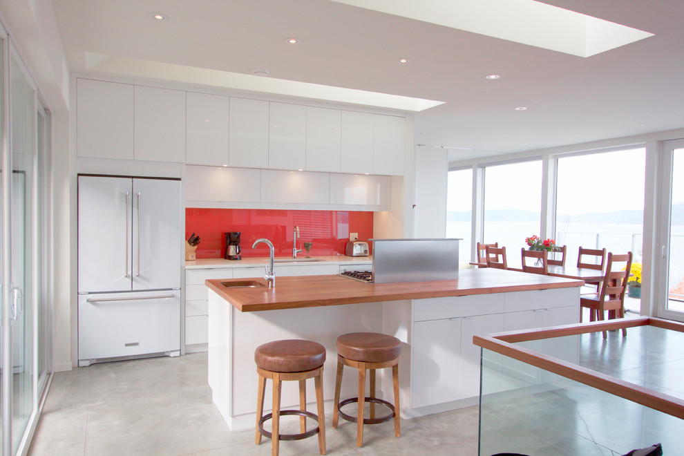 Idéer för ett mellanstort modernt brun linjärt kök och matrum, med en undermonterad diskho, släta luckor, vita skåp, träbänkskiva, rött stänkskydd, glaspanel som stänkskydd, vita vitvaror, betonggolv, en köksö och grått golv