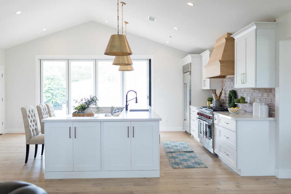 Inspiration for a large traditional galley kitchen/diner in Phoenix with a submerged sink, shaker cabinets, engineered stone countertops, brick splashback, stainless steel appliances, white worktops, white cabinets, brown splashback, medium hardwood flooring, an island and brown floors.