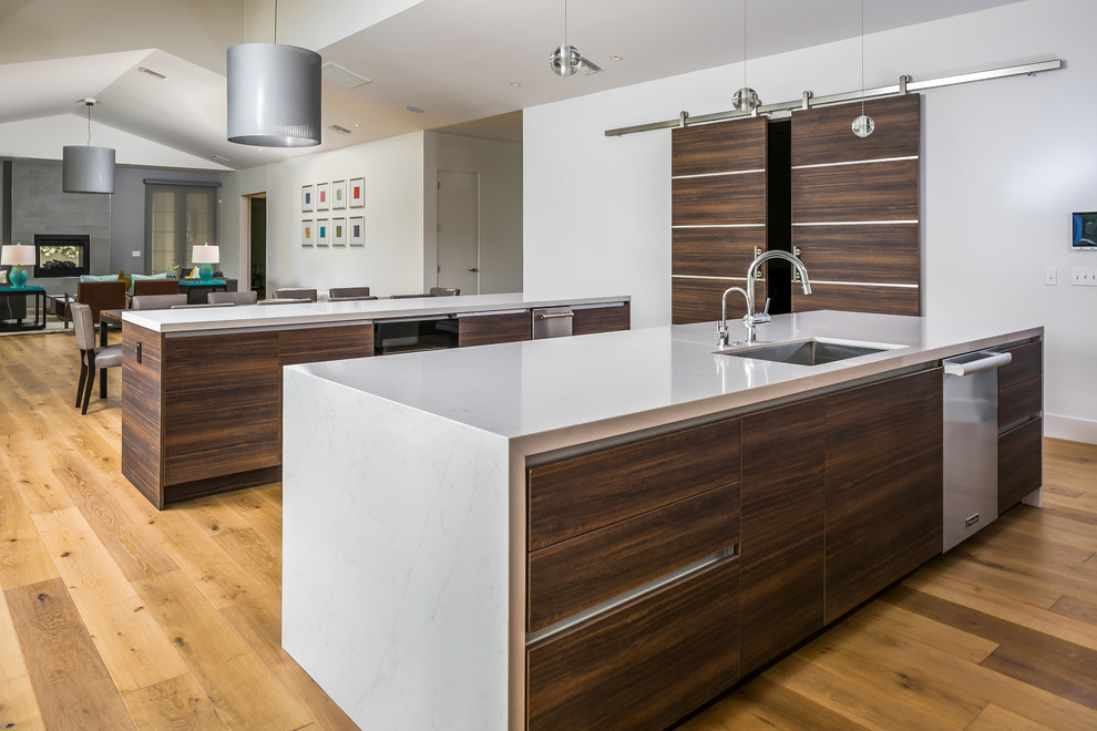 Photo of an expansive contemporary single-wall open plan kitchen in Phoenix with a submerged sink, flat-panel cabinets, dark wood cabinets, engineered stone countertops, white splashback, stainless steel appliances, light hardwood flooring, multiple islands, brown floors and white worktops.