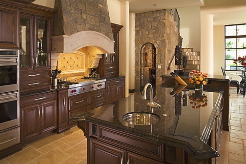 Inspiration for a mediterranean l-shaped open concept kitchen remodel in Phoenix with an undermount sink, raised-panel cabinets, dark wood cabinets, granite countertops, beige backsplash and stainless steel appliances