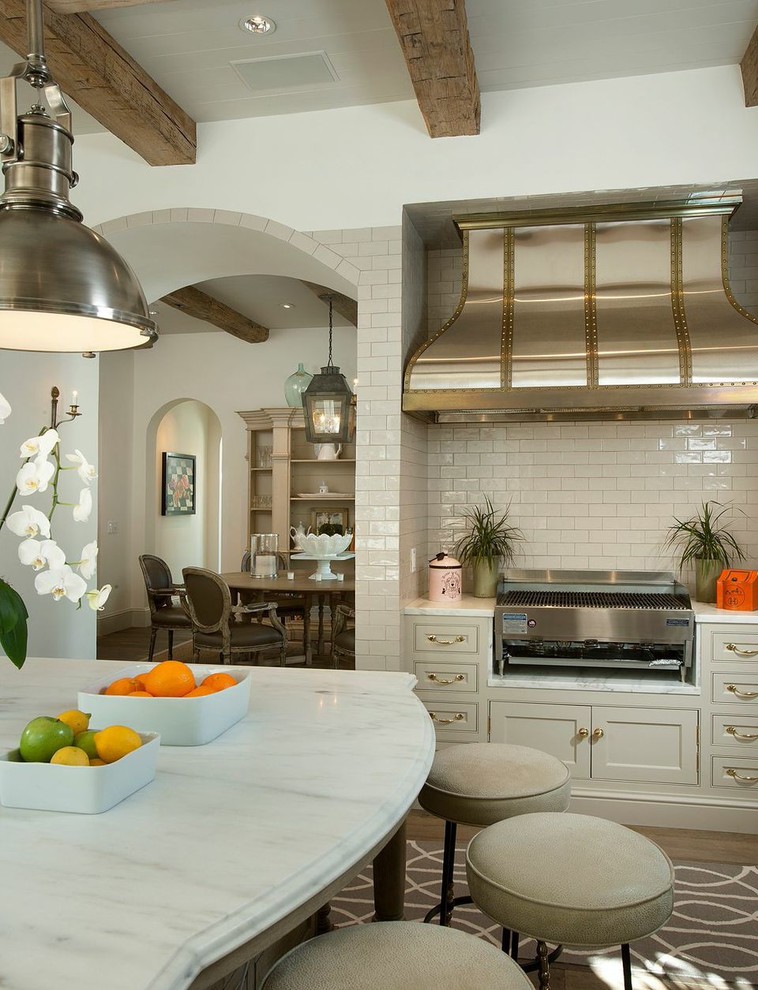 フェニックスにある地中海スタイルのおしゃれなアイランドキッチン (シェーカースタイル扉のキャビネット、ベージュのキャビネット、白いキッチンパネル、サブウェイタイルのキッチンパネル、濃色無垢フローリング) の写真