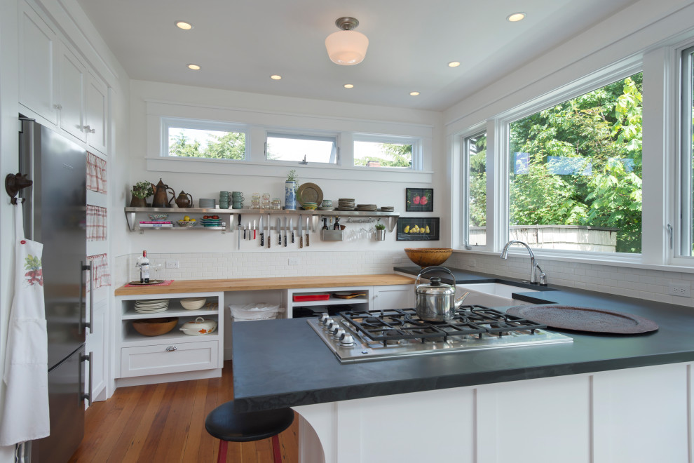 Inspiration for a mid-sized transitional u-shaped medium tone wood floor and brown floor eat-in kitchen remodel in Seattle with a farmhouse sink, recessed-panel cabinets, white cabinets, soapstone countertops, white backsplash, cement tile backsplash, stainless steel appliances, a peninsula and black countertops