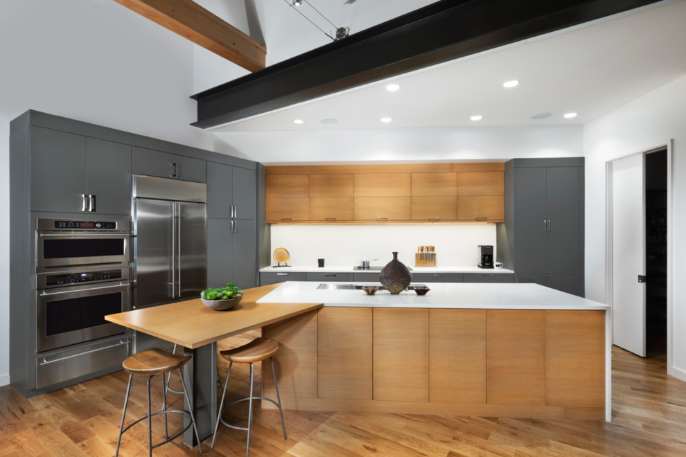 Идея дизайна: параллельная кухня в современном стиле с плоскими фасадами, серыми фасадами, техникой из нержавеющей стали, паркетным полом среднего тона, островом и коричневым полом