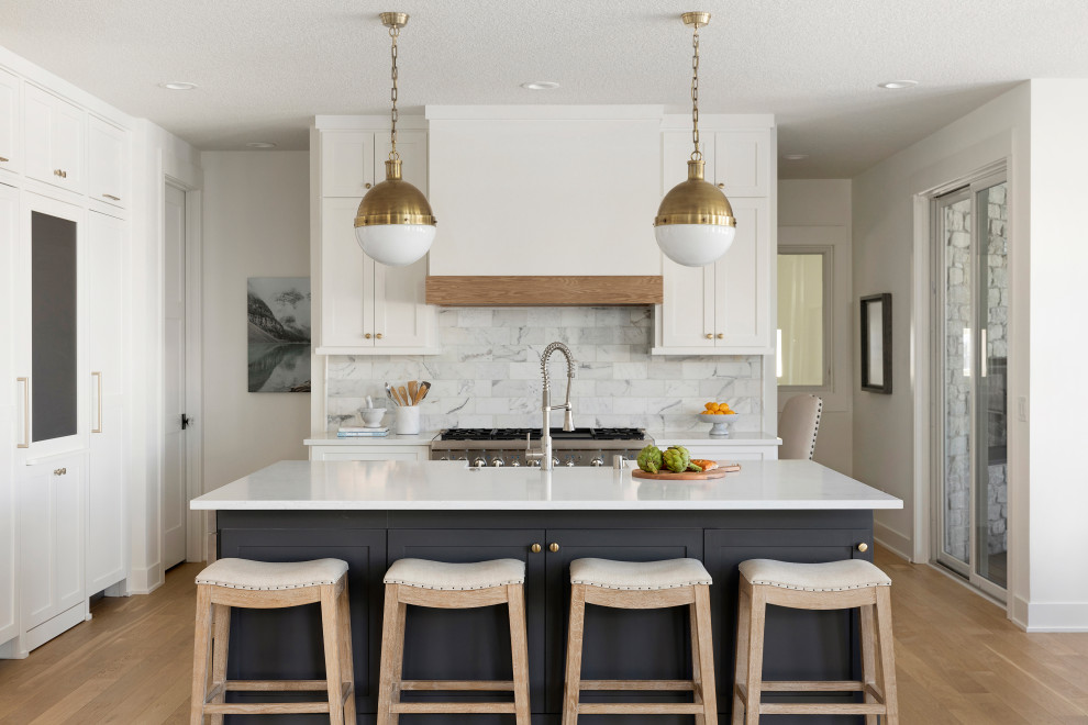 Design ideas for a transitional kitchen in Minneapolis with white cabinets, quartzite benchtops, marble splashback, stainless steel appliances, light hardwood floors and with island.