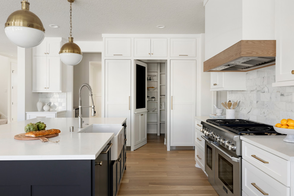 Foto de cocina clásica renovada con puertas de armario blancas, encimera de cuarcita, salpicadero de mármol, electrodomésticos de acero inoxidable, suelo de madera clara y una isla