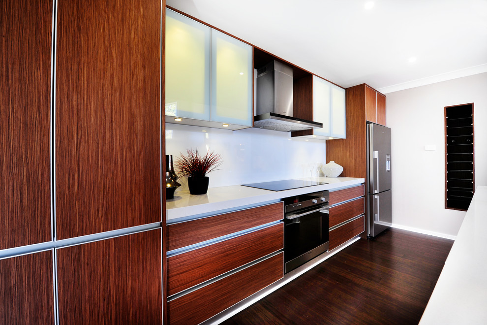 Example of a small trendy galley bamboo floor eat-in kitchen design in Central Coast with an undermount sink, glass-front cabinets, medium tone wood cabinets, quartz countertops, white backsplash, glass sheet backsplash, stainless steel appliances and an island