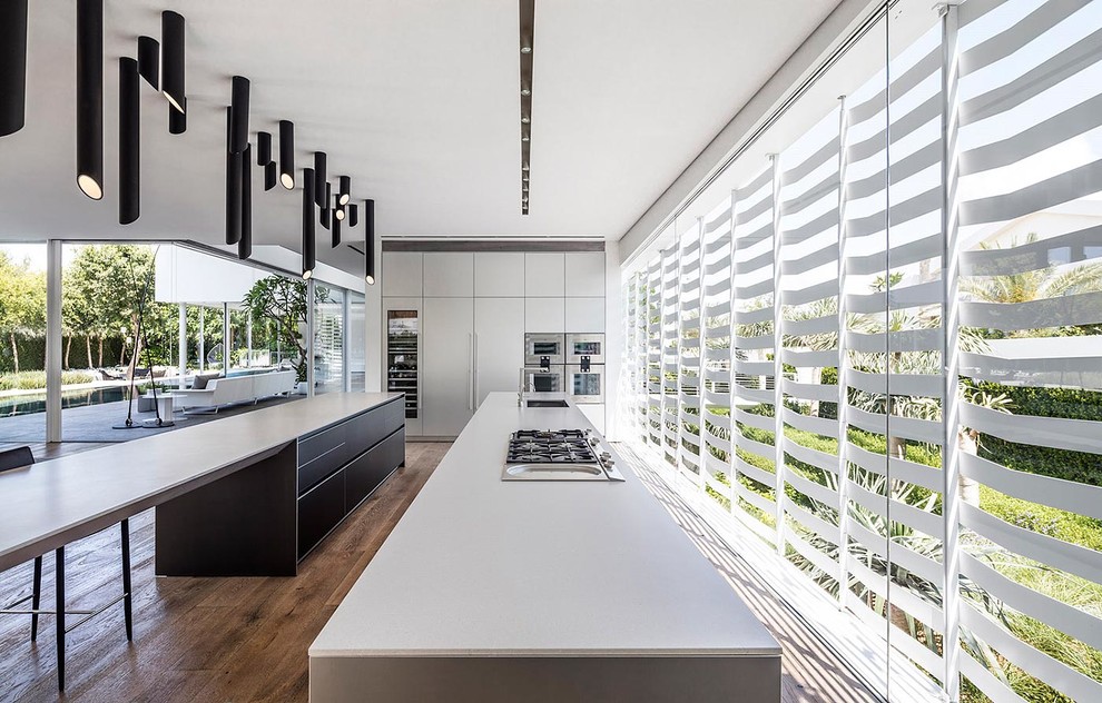 Expansive contemporary open plan kitchen in Other with flat-panel cabinets, white cabinets, stainless steel appliances, medium hardwood flooring, multiple islands, a submerged sink and quartz worktops.