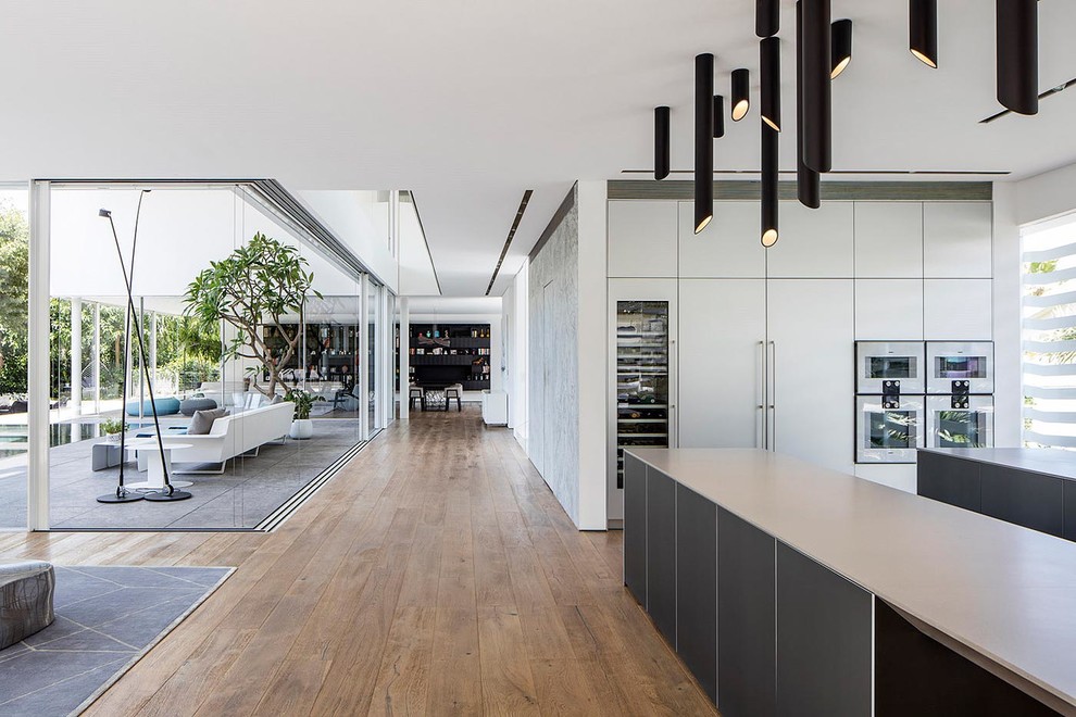 Photo of an expansive modern single-wall open plan kitchen in London with an integrated sink, flat-panel cabinets, white cabinets, engineered stone countertops, light hardwood flooring and multiple islands.