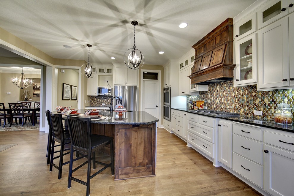 Example of a large arts and crafts l-shaped medium tone wood floor open concept kitchen design in Minneapolis with beaded inset cabinets, white cabinets, granite countertops, ceramic backsplash, stainless steel appliances and an island