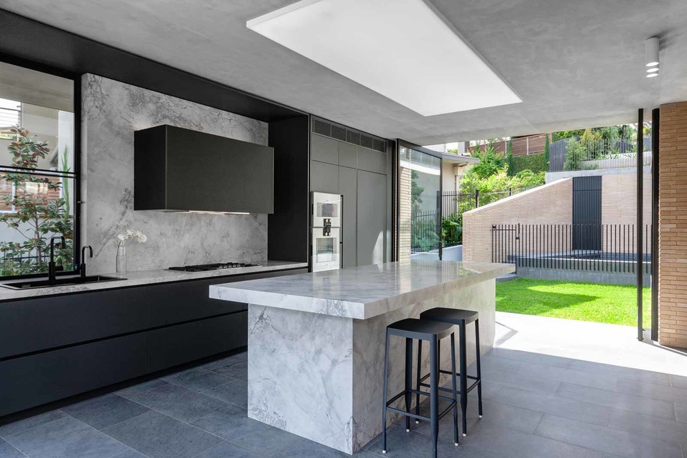 Large contemporary galley kitchen/diner in Sydney with a submerged sink, black cabinets, marble worktops, grey splashback, marble splashback, stainless steel appliances, an island, grey floors and grey worktops.