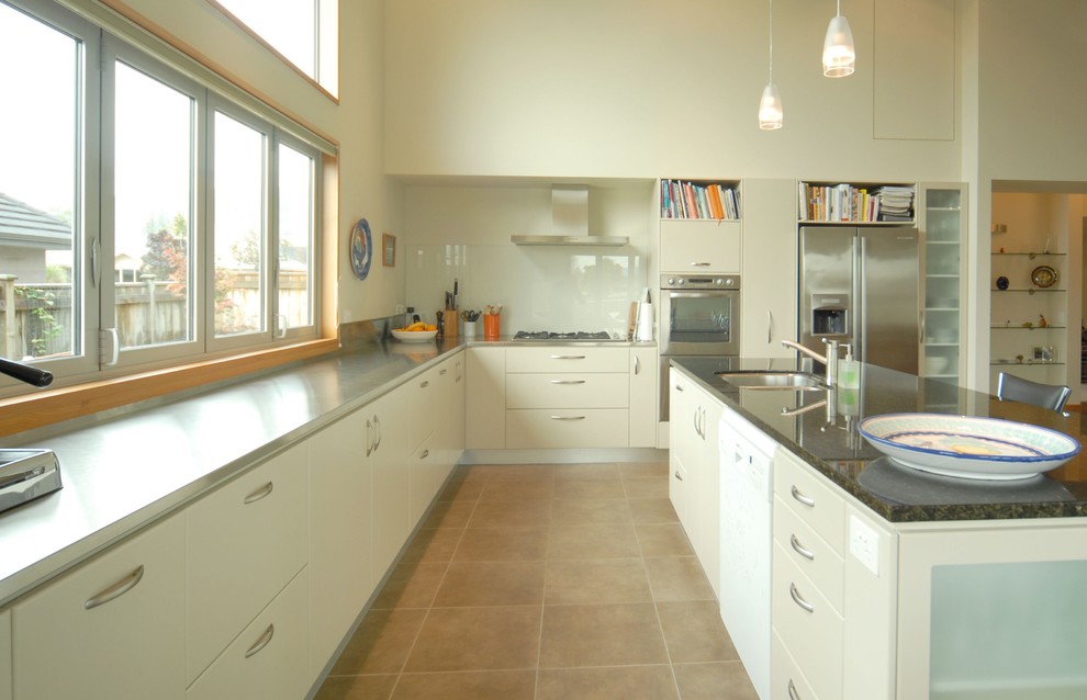 Foto på ett stort funkis kök, med en undermonterad diskho, släta luckor, beige skåp, bänkskiva i rostfritt stål, beige stänkskydd, glaspanel som stänkskydd, rostfria vitvaror, klinkergolv i porslin och en köksö