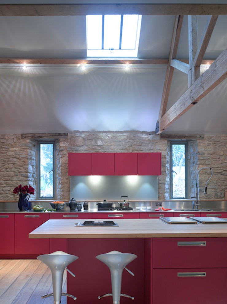 Modern inredning av ett stort kök med öppen planlösning, med en undermonterad diskho, släta luckor, röda skåp, bänkskiva i rostfritt stål, stänkskydd med metallisk yta, rostfria vitvaror och en köksö
