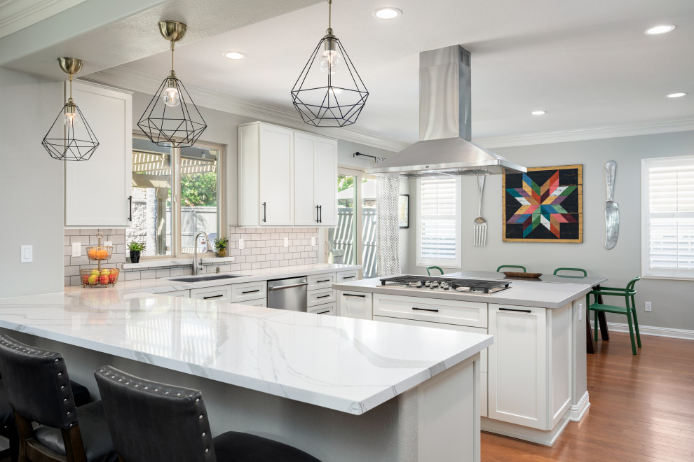 Transitional l-shaped medium tone wood floor and brown floor kitchen photo in San Diego with an undermount sink, shaker cabinets, white cabinets, white backsplash, subway tile backsplash, stainless steel appliances, an island and white countertops