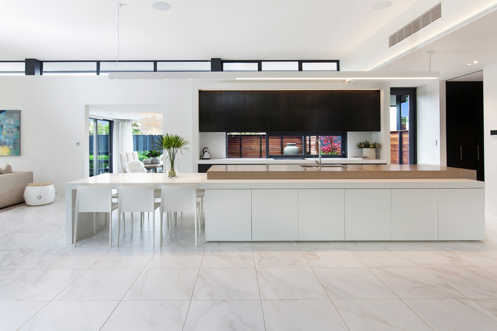 Kitchen - contemporary galley marble floor and white floor kitchen idea in Christchurch with an undermount sink, flat-panel cabinets, white cabinets, paneled appliances, an island and beige countertops