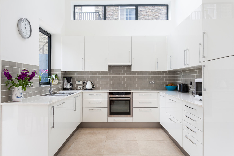 Design ideas for a contemporary u-shaped kitchen in London with a submerged sink, flat-panel cabinets, white cabinets, grey splashback, metro tiled splashback, stainless steel appliances and no island.