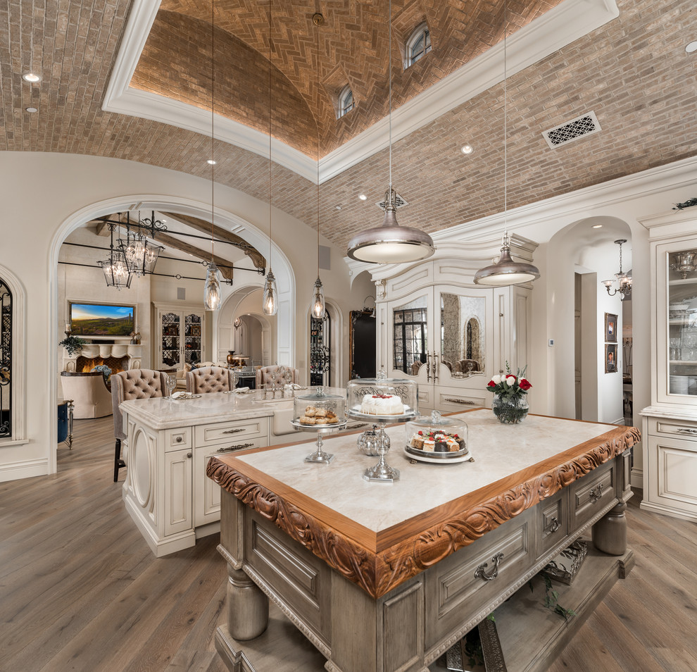 Inspiration for a huge modern u-shaped dark wood floor and brown floor enclosed kitchen remodel in Phoenix with a farmhouse sink, raised-panel cabinets, light wood cabinets, quartzite countertops, multicolored backsplash, porcelain backsplash, stainless steel appliances, two islands and beige countertops