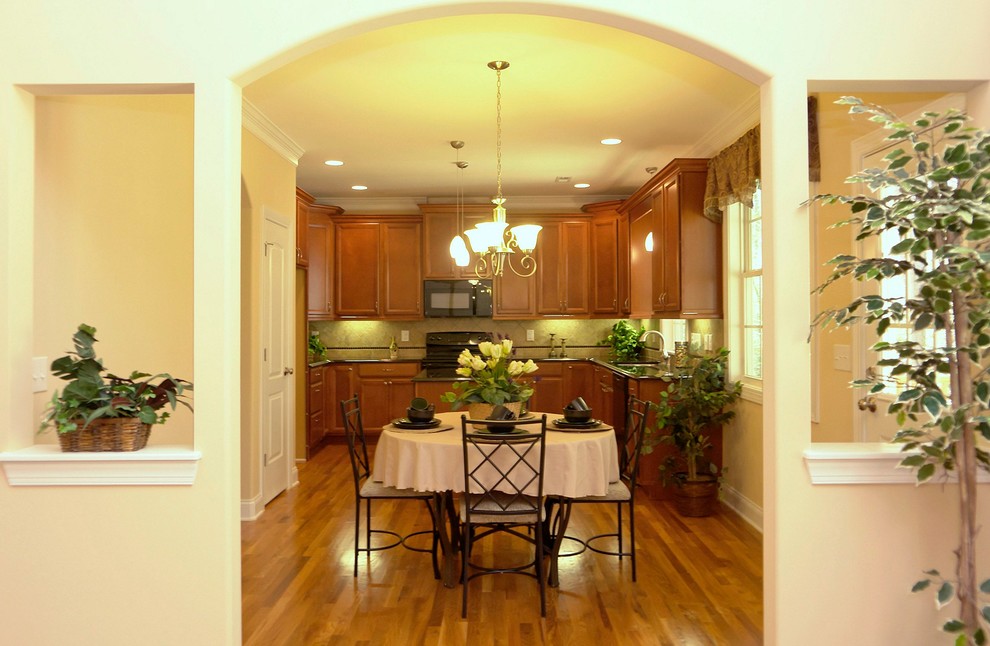 Example of a mid-sized classic u-shaped light wood floor enclosed kitchen design in Raleigh with a double-bowl sink, recessed-panel cabinets, medium tone wood cabinets, granite countertops, black backsplash, ceramic backsplash, black appliances and an island