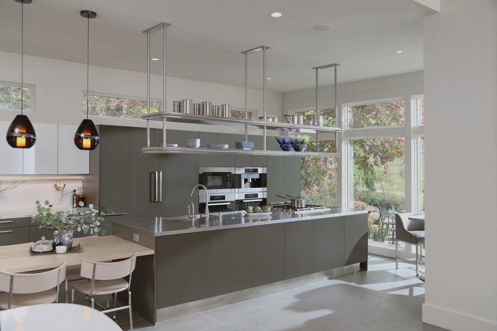 Modern inredning av ett stort kök, med en integrerad diskho, släta luckor, grå skåp, bänkskiva i rostfritt stål, vitt stänkskydd, stänkskydd i marmor, integrerade vitvaror, en köksö och grått golv