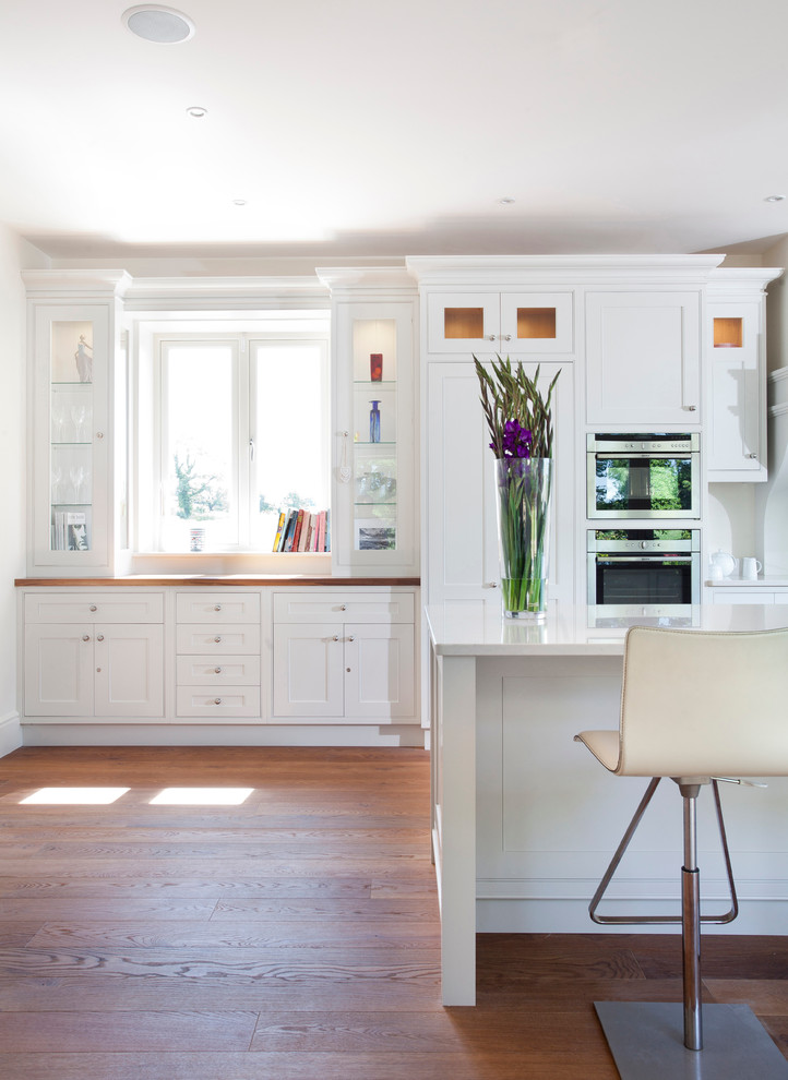 Foto på ett mellanstort funkis kök, med en undermonterad diskho, luckor med profilerade fronter, vita skåp, bänkskiva i kvarts, stänkskydd i sten, rostfria vitvaror, mellanmörkt trägolv och en köksö