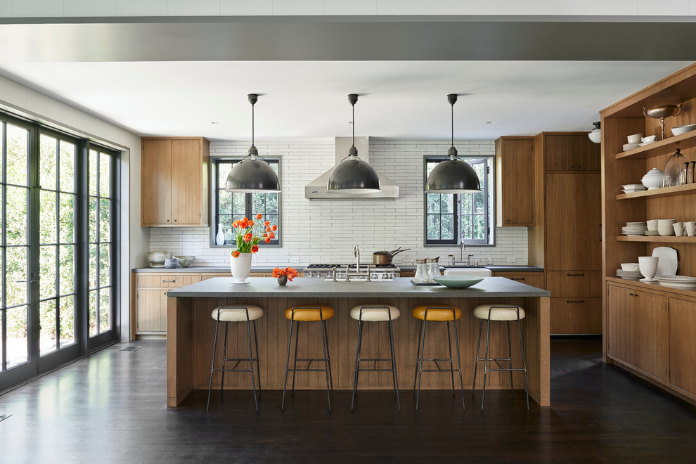 Diseño de cocina actual con armarios con paneles lisos, puertas de armario de madera oscura, salpicadero blanco, electrodomésticos de acero inoxidable, suelo de madera oscura, una isla y encimera de granito