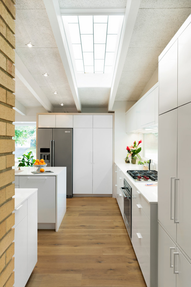 Idéer för ett avskilt, stort modernt u-kök, med en undermonterad diskho, släta luckor, vita skåp, bänkskiva i kvarts, fönster som stänkskydd, rostfria vitvaror, mellanmörkt trägolv, en köksö och brunt golv